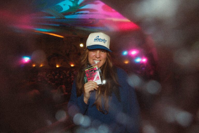 Image of a girl wearing a hat with a festival pass in her mouth